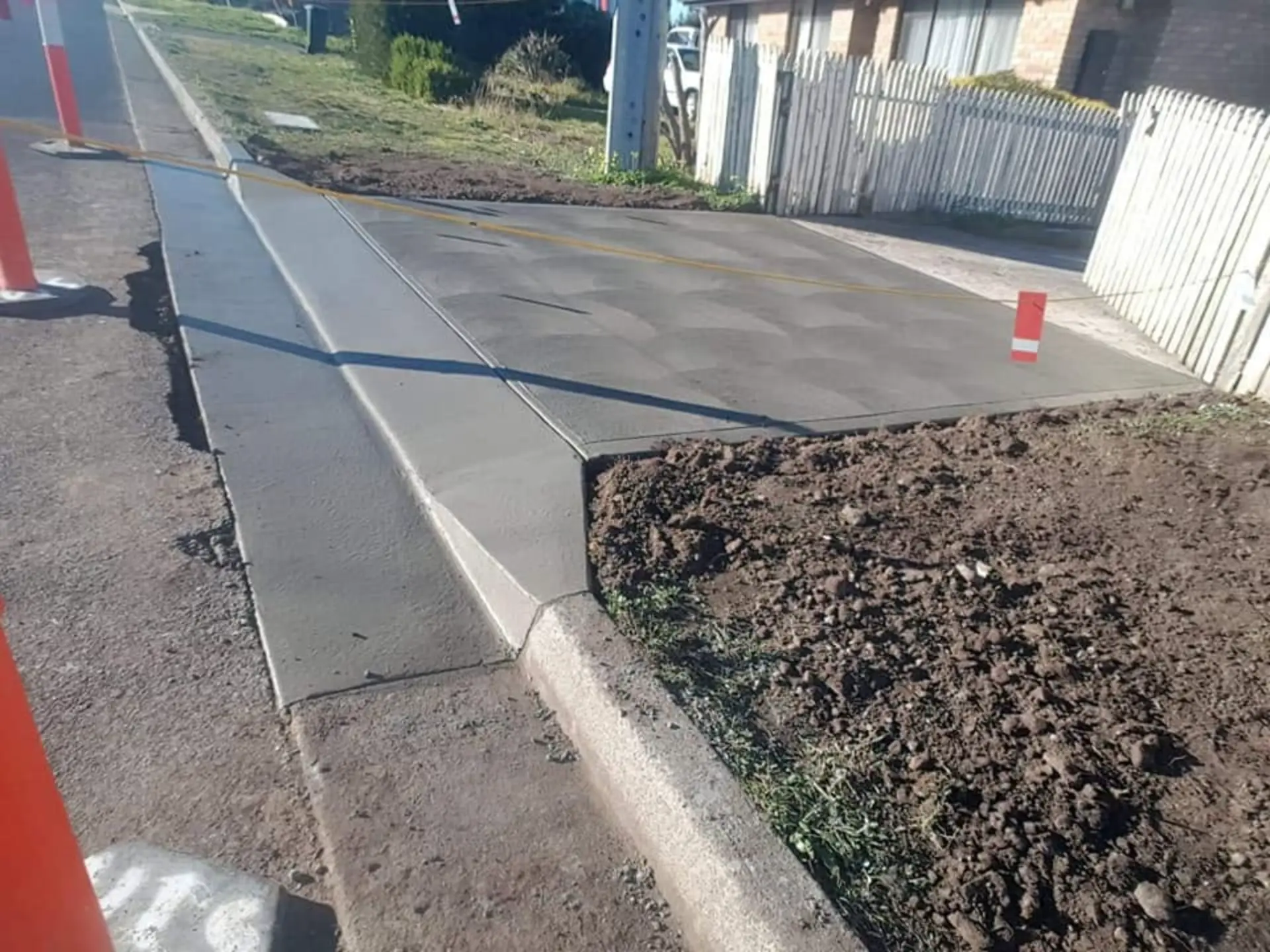 A finished concrete crossover and path against a fenced street verge