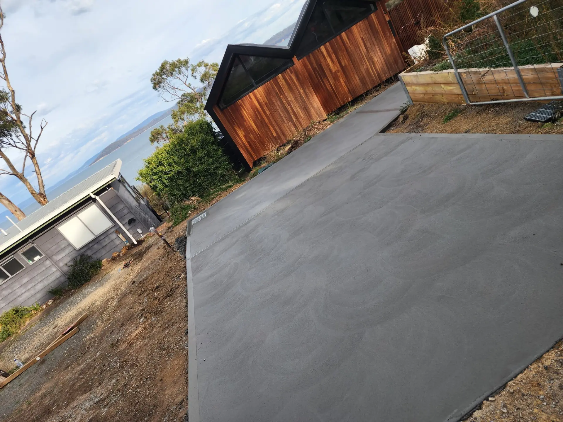 A large finished concrete slab laid beside a dark house and timber fence
