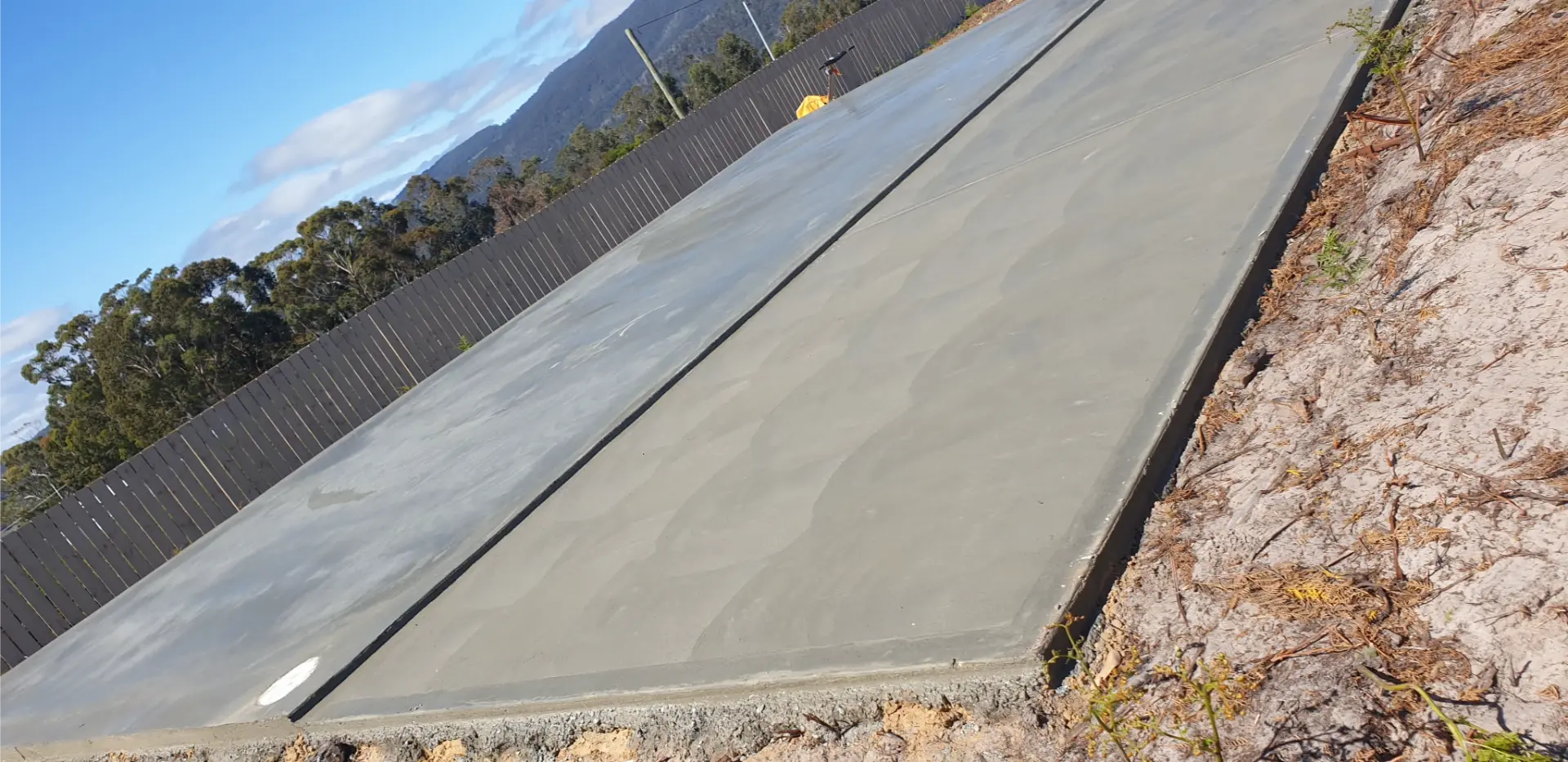 A finished concrete pad with a crisp formed edge, fence line and hills behind