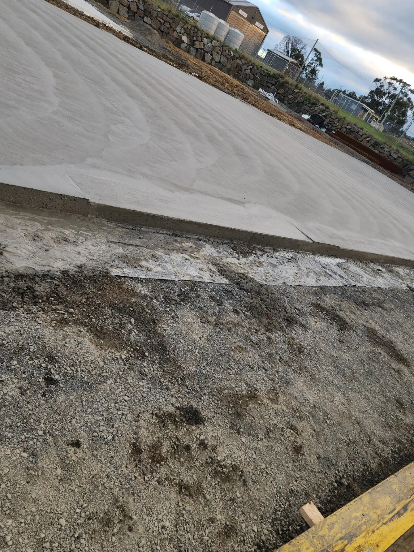 A broad freshly screeded concrete pad sitting above dark graded fill on an open block
