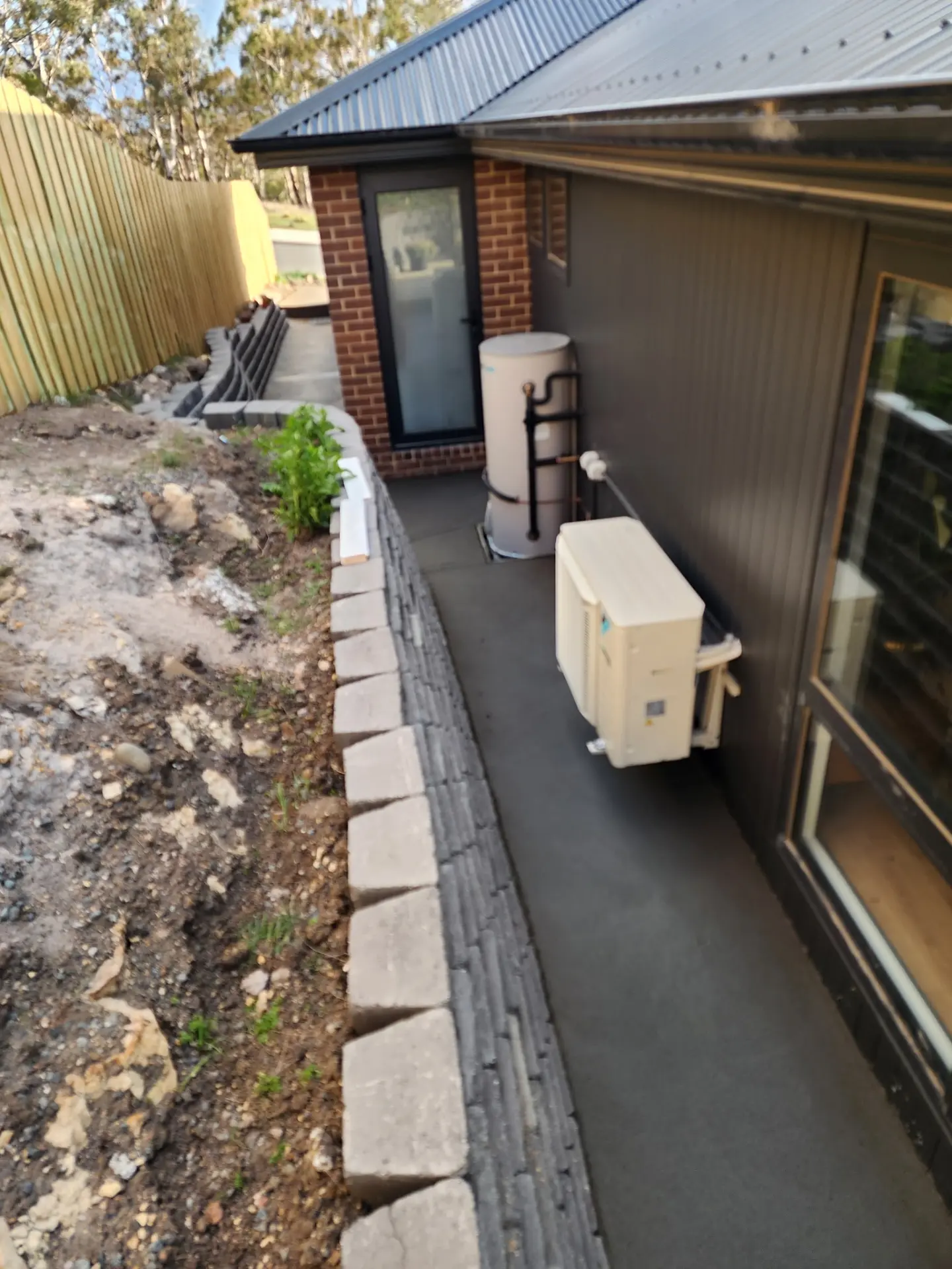 A concrete path running along the side of a home past a block retaining wall