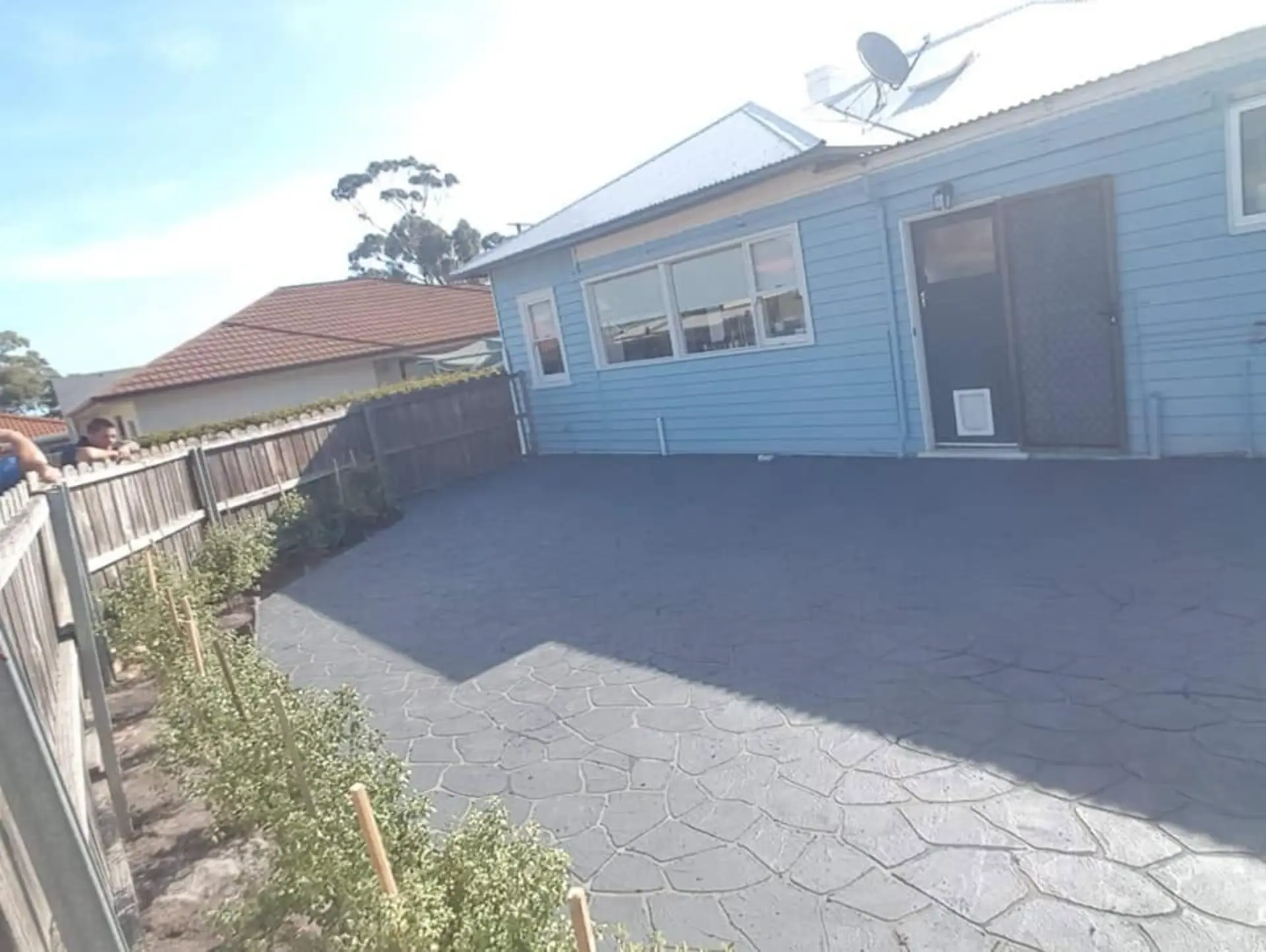 A finished driveway and turning area beside a blue weatherboard home