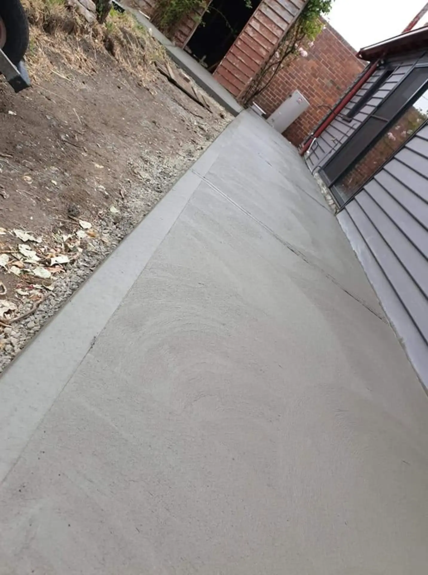 A steep concrete ramp path poured between a house wall and retaining rock
