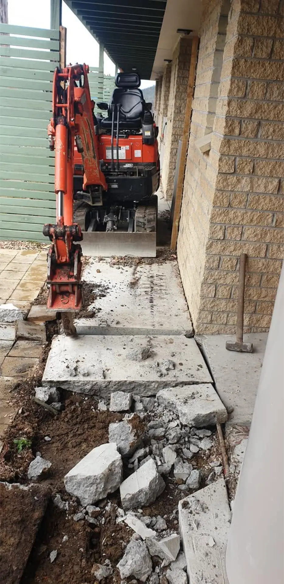 An excavator cutting in the base for a new concrete path beside a house