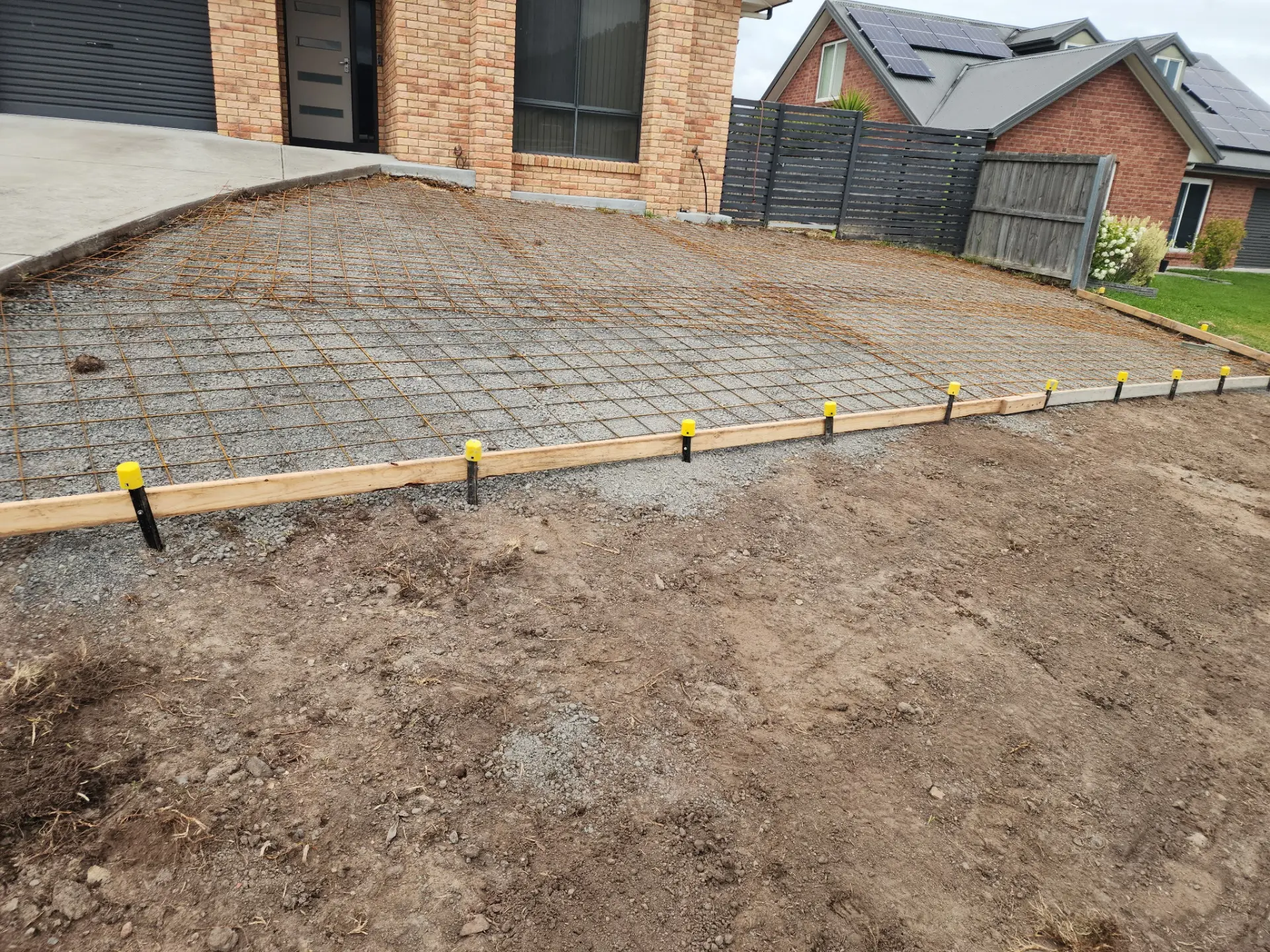 Reinforcing mesh and timber formwork set over a prepared pad behind a brick house