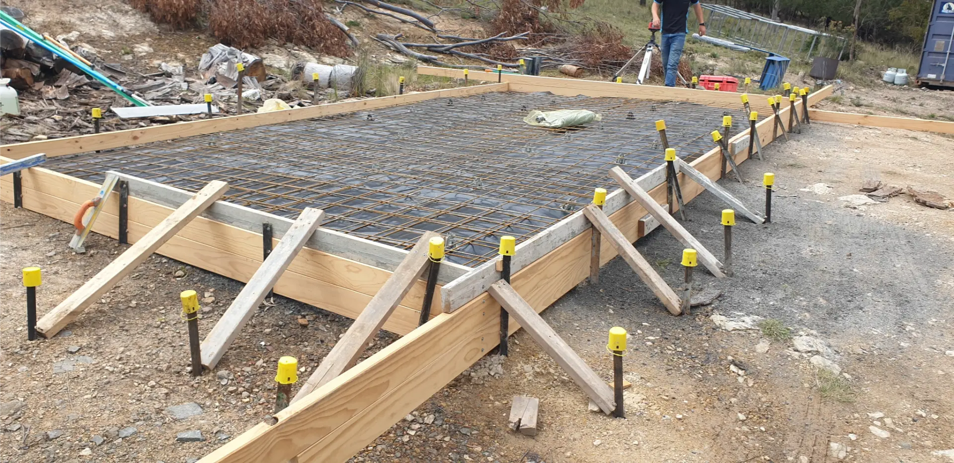 Timber formwork and reinforcing mesh set out on a prepared pad with yellow-capped starter bars