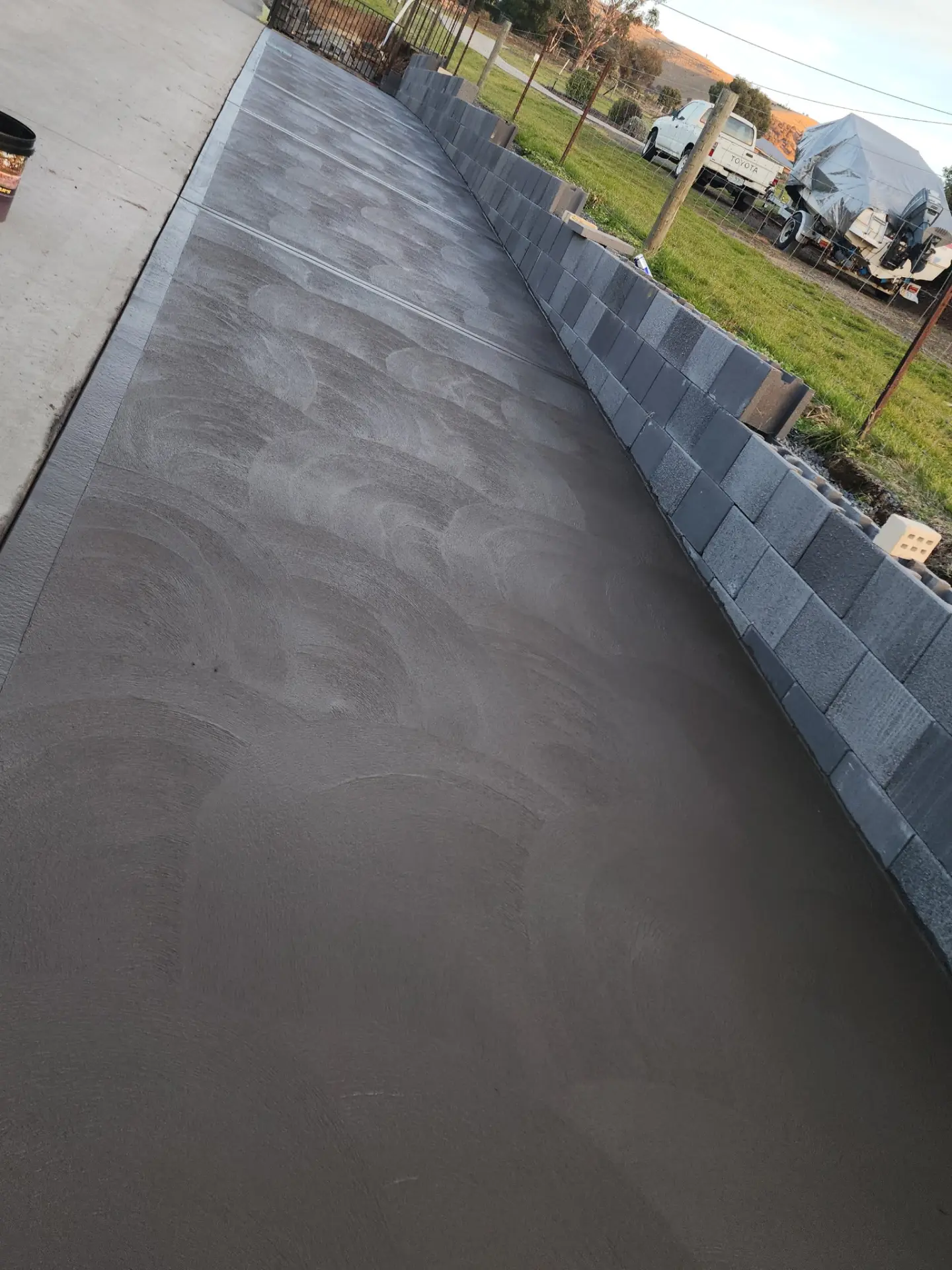 A wide finished concrete path running between a block retaining wall and an open yard