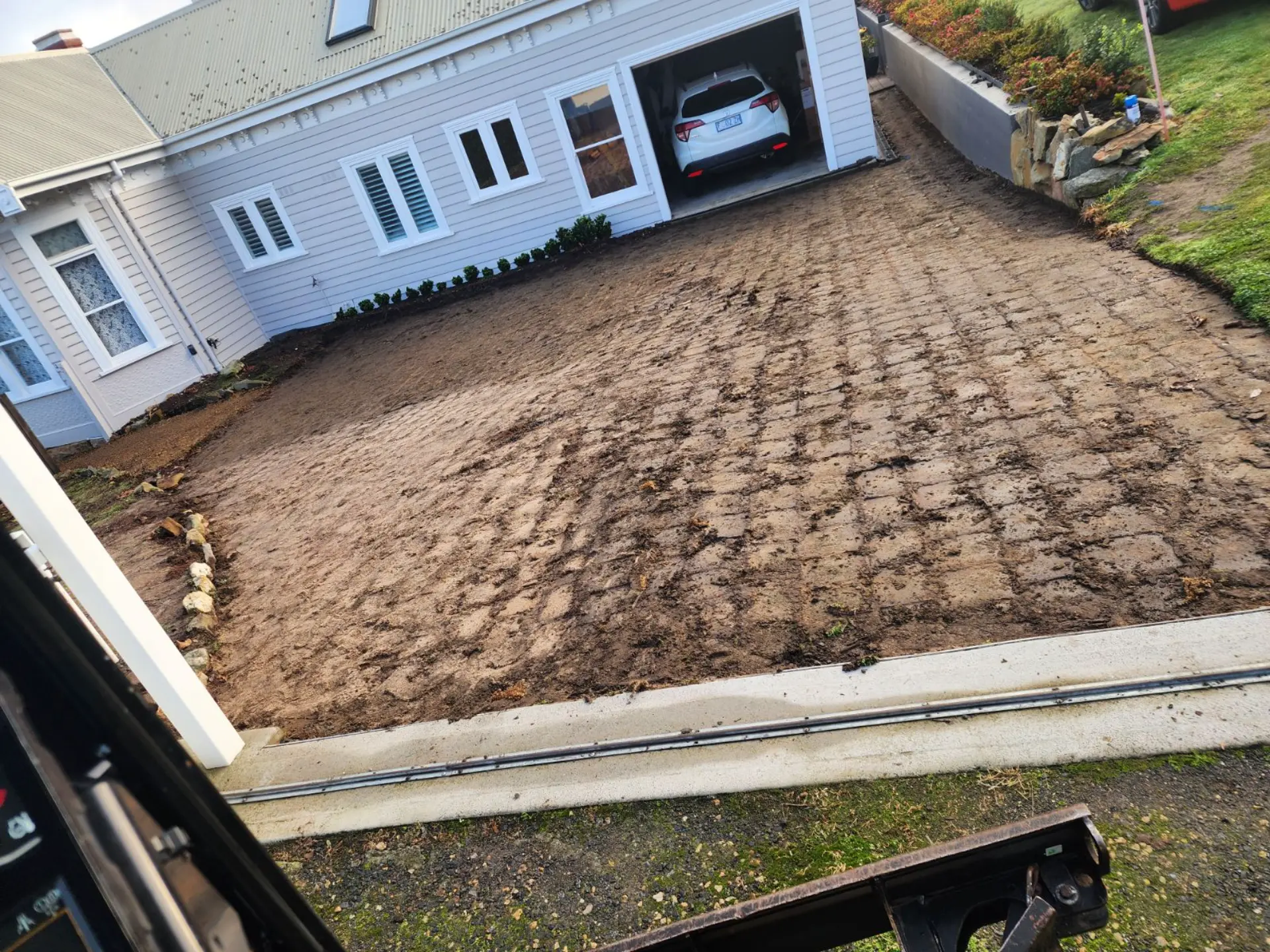 A driveway area excavated and graded ready for concrete in front of a white home and garage