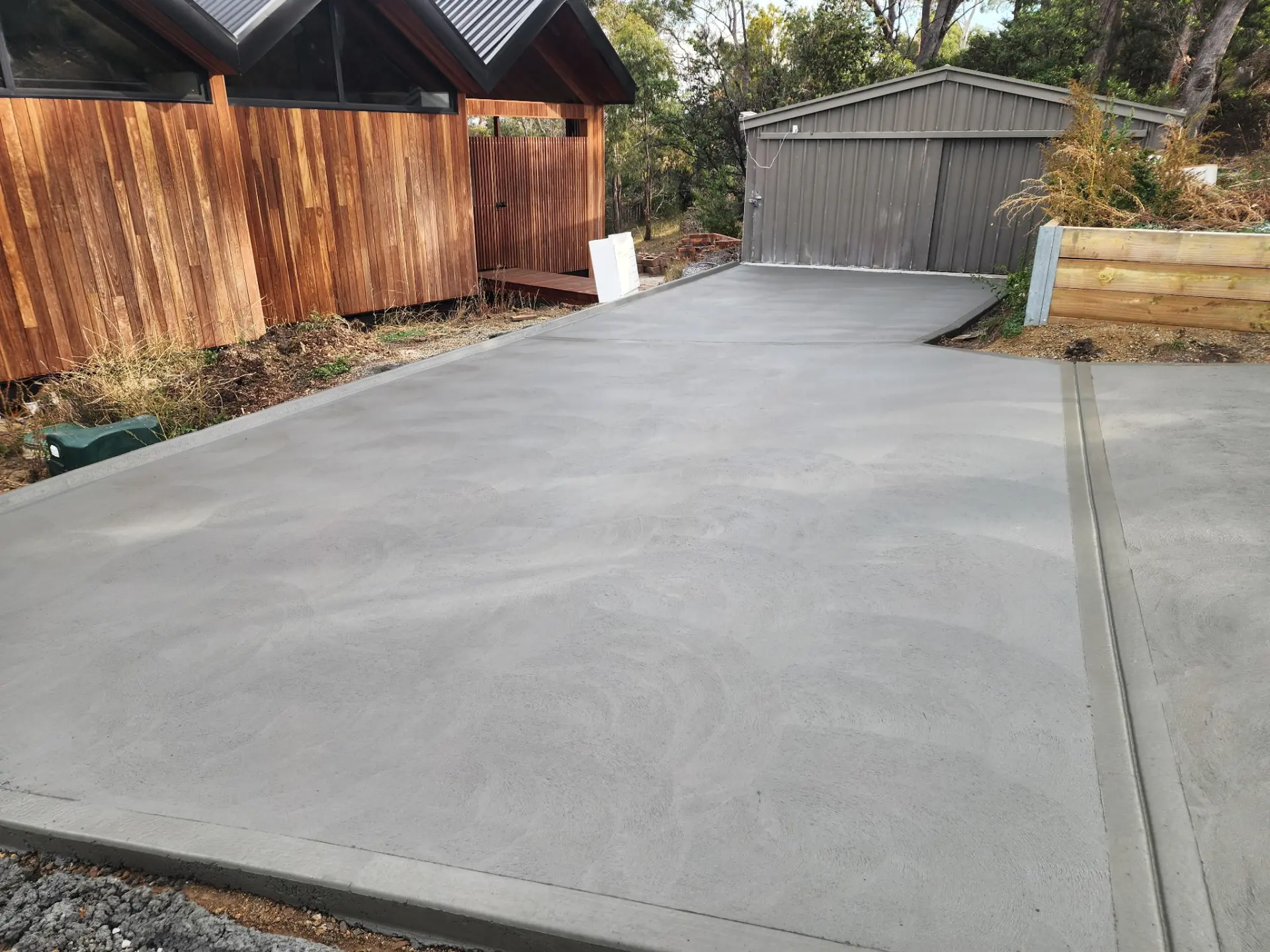 A wide finished concrete driveway running past a timber fence up to a garage