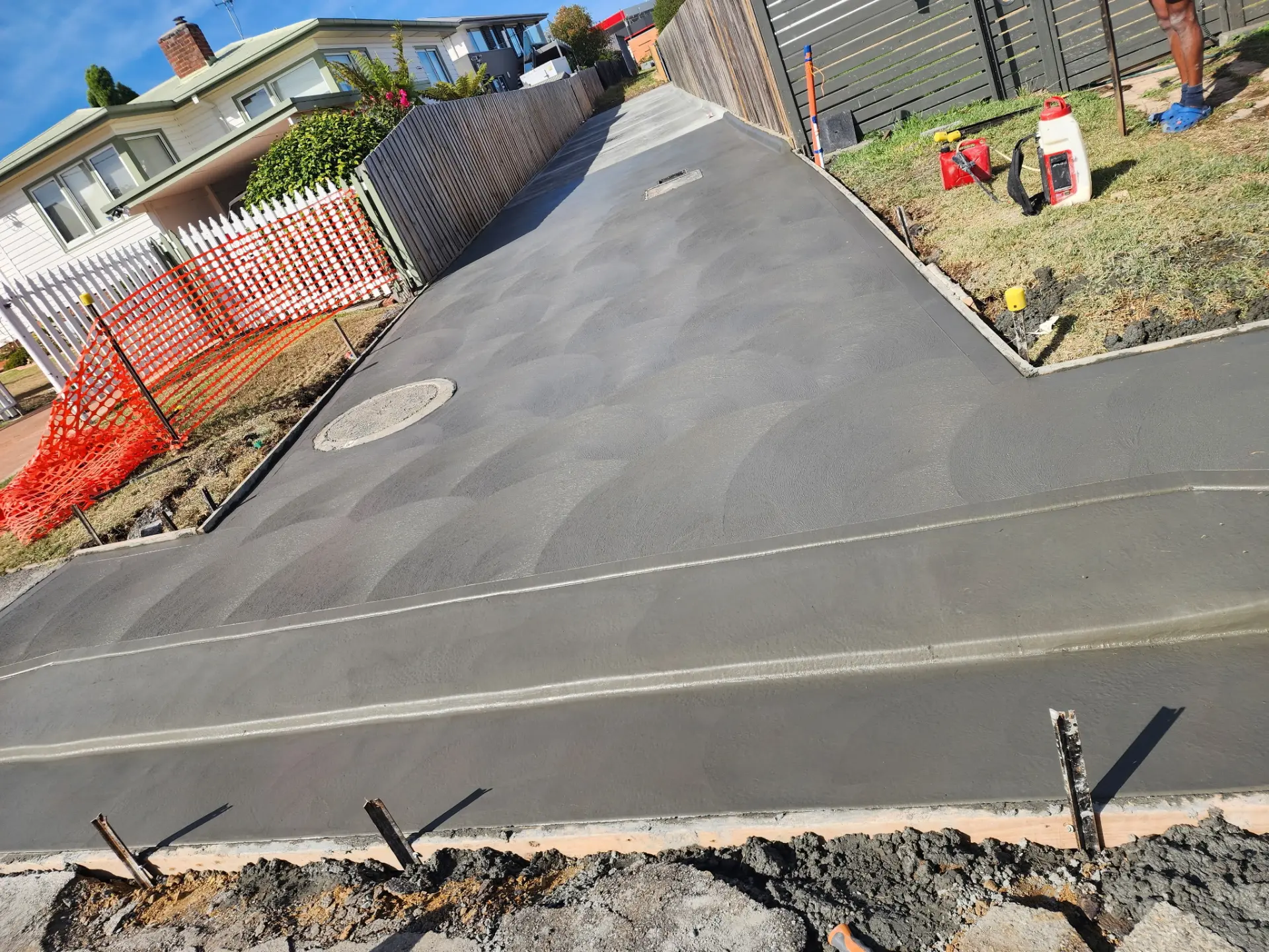 A fresh concrete driveway poured out to the street with edge pegs and temporary safety fencing