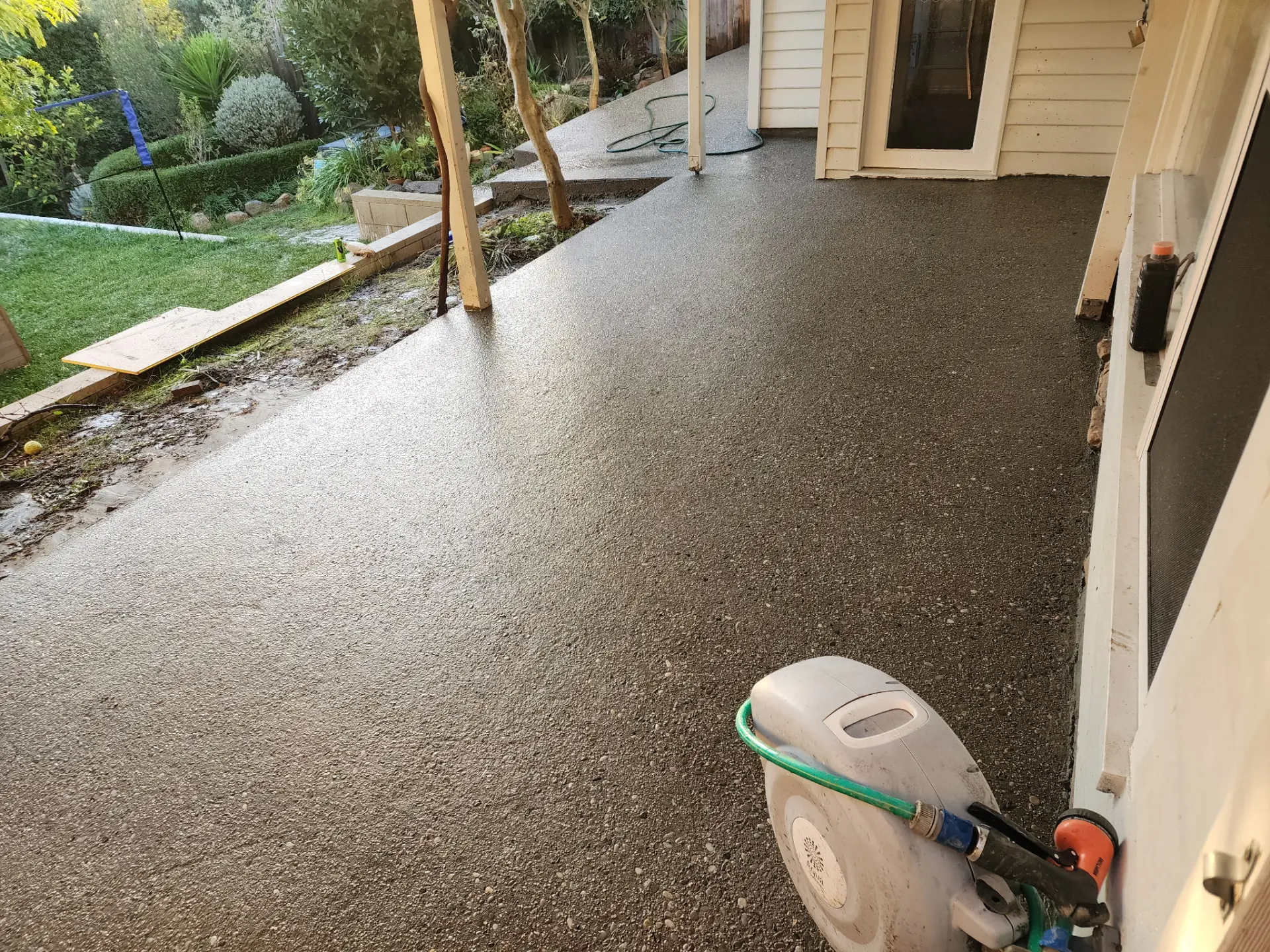 An exposed aggregate path being washed back beside a cream weatherboard house and garden