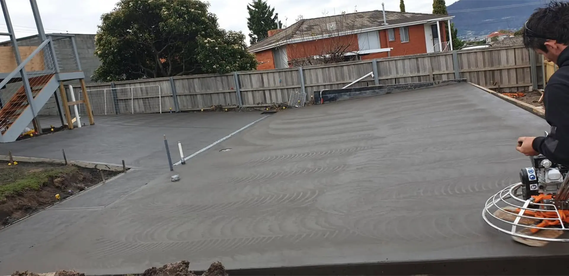 A concreter power floating a freshly poured residential backyard slab behind a suburban home