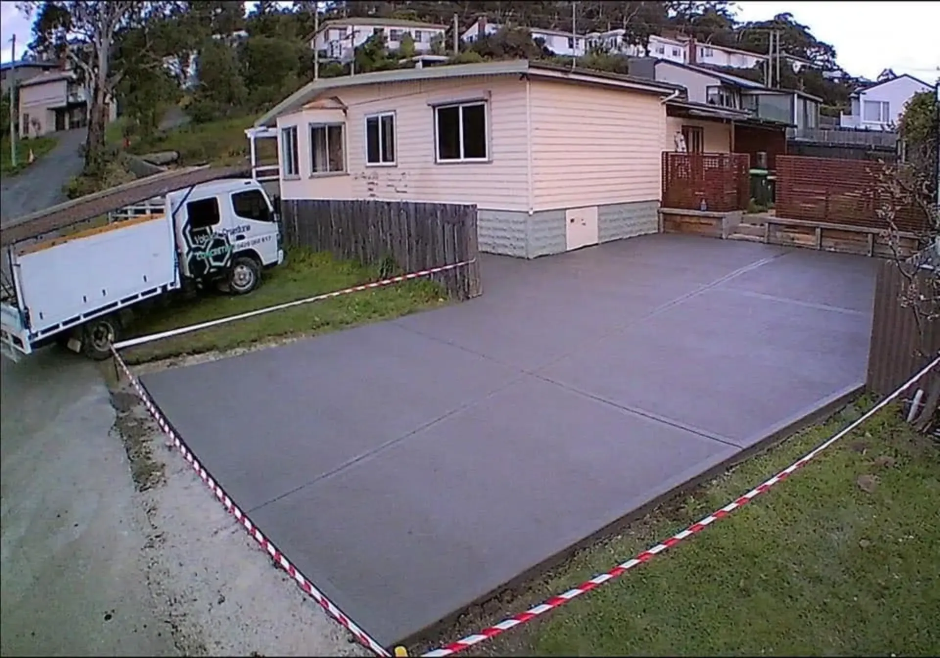 A large plain-finish driveway apron poured in front of a house and tape barrier