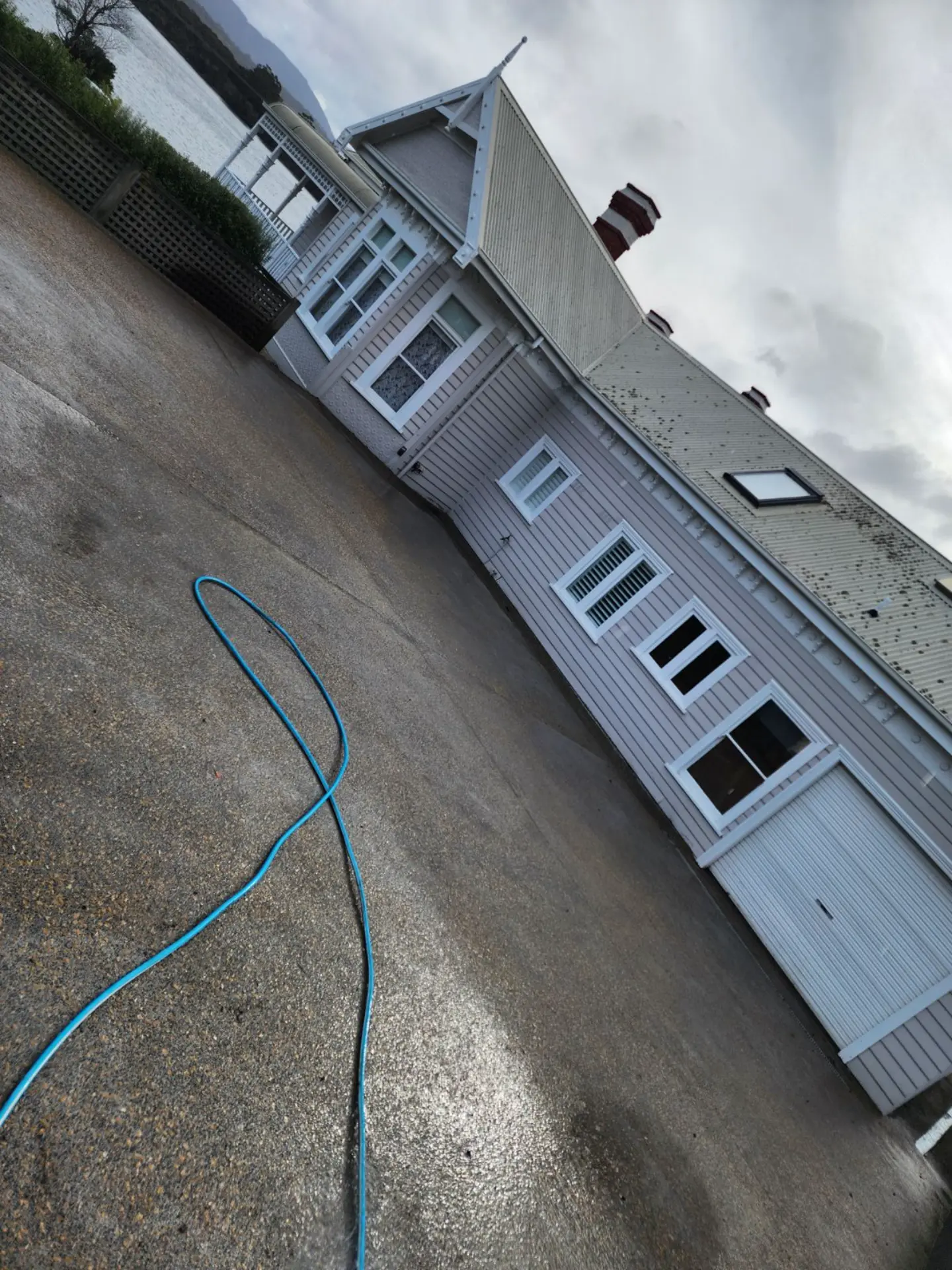 A hose lying across a freshly washed exposed aggregate driveway beside a white weatherboard house