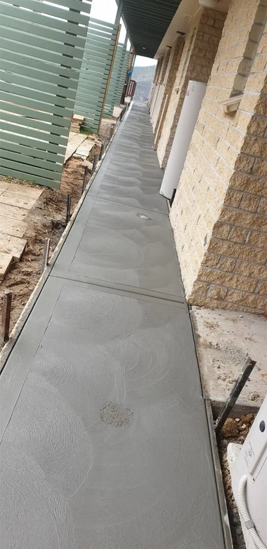 A poured side path between a brick wall and a colorbond fence, trowelled smooth