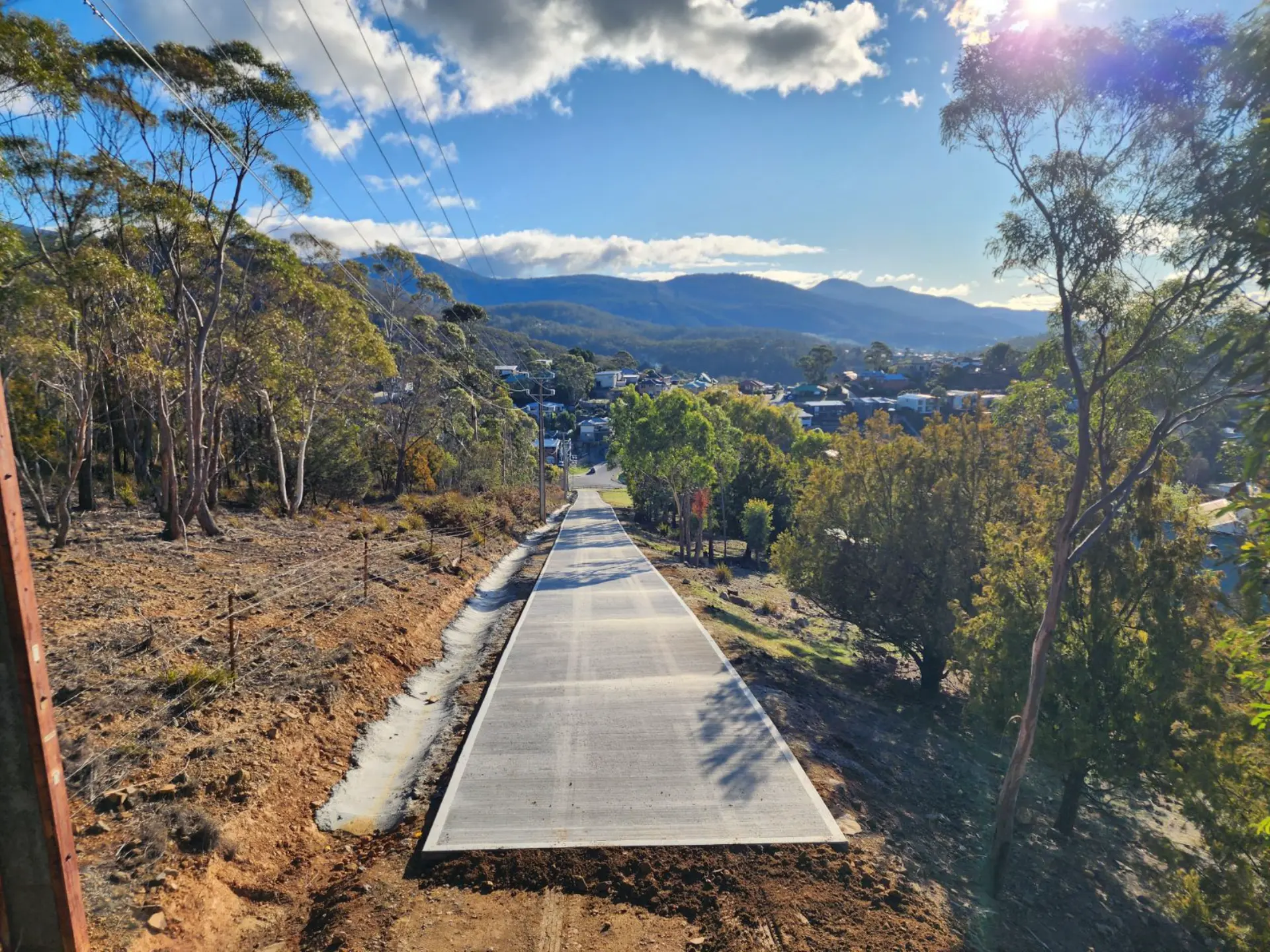A long concrete driveway running downhill through bush toward a valley township