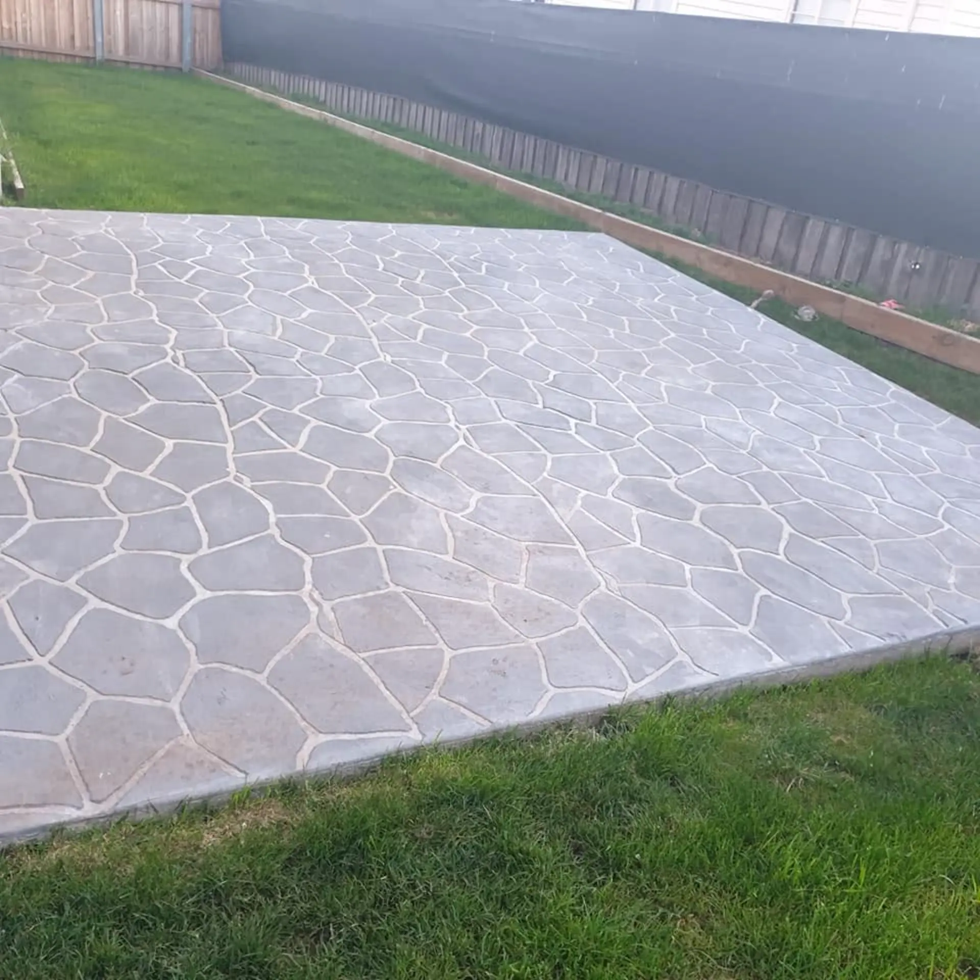 A stamped decorative patio finished against a fence and lawn