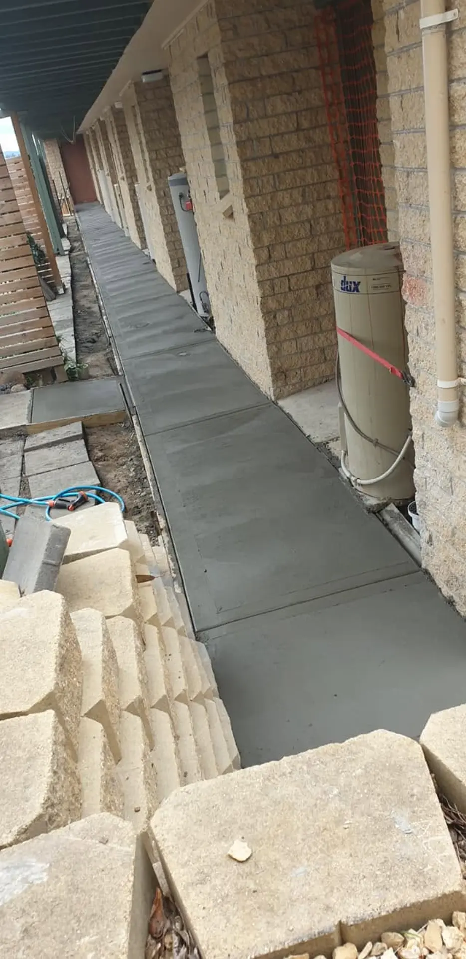 A long finished concrete path running down the side of a cream brick house