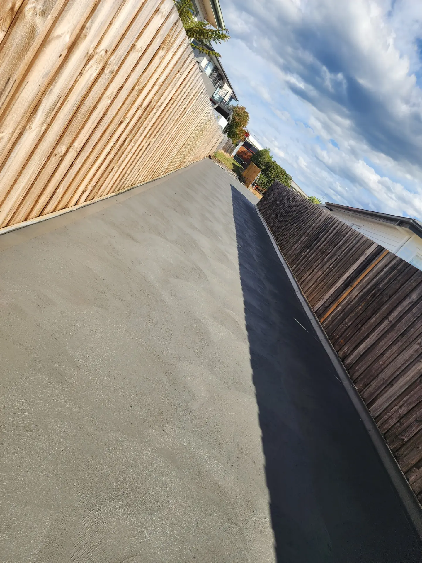 A fresh concrete strip poured between a new timber fence and an older paling fence