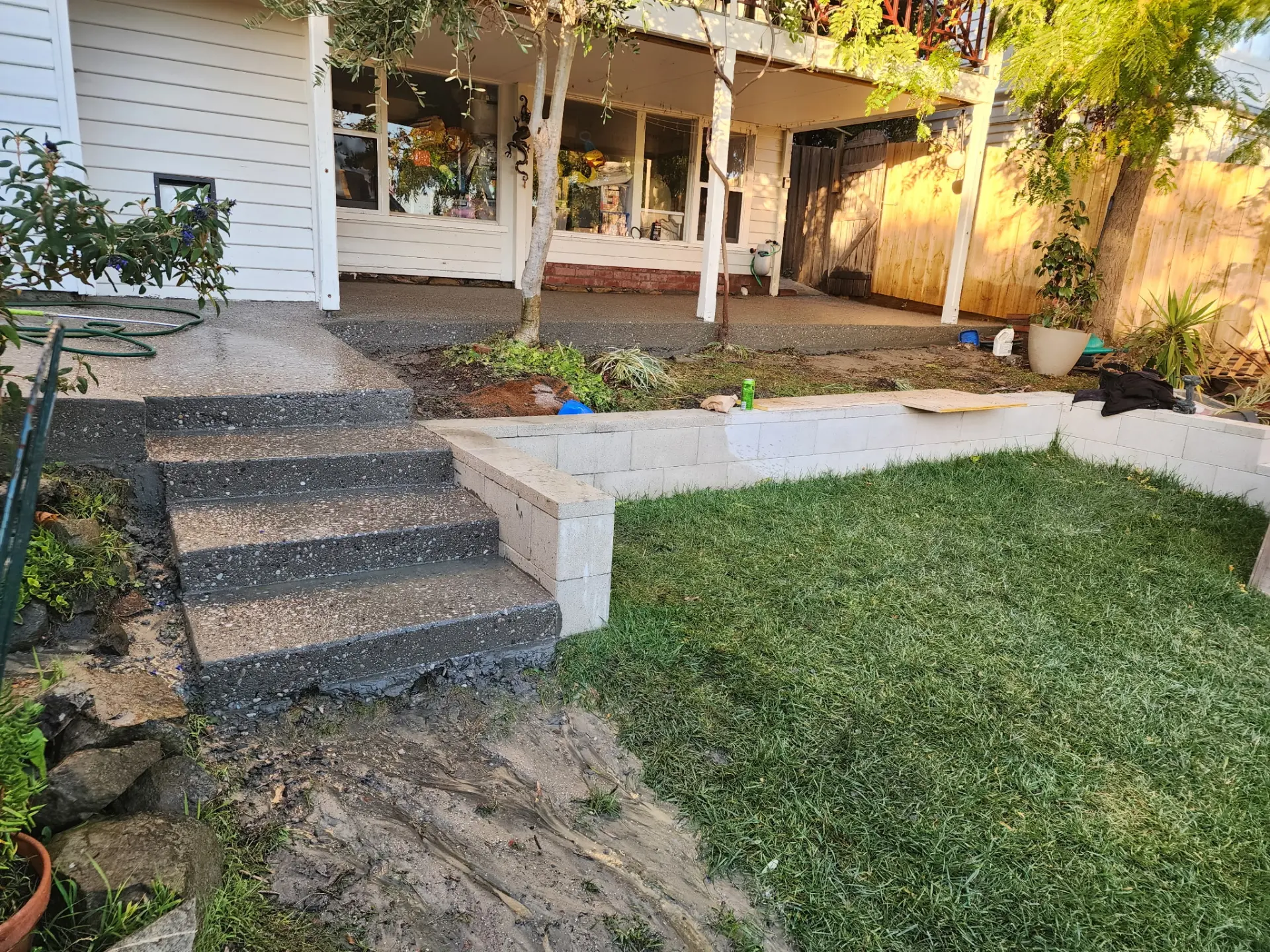 Exposed aggregate steps rising from a lawn to a covered verandah beside a block garden wall