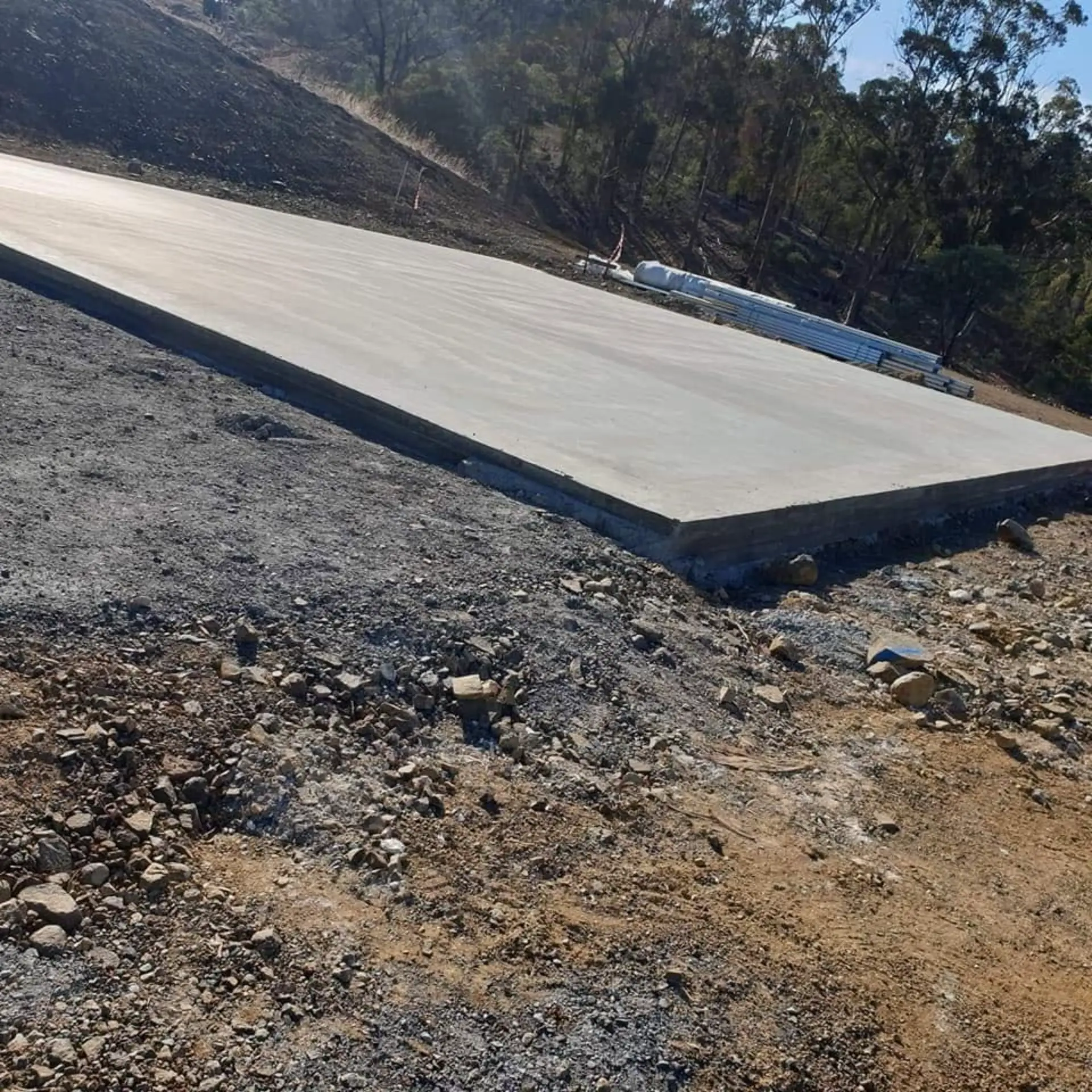 A wide shed pad slab finished on a rock-strewn rural site
