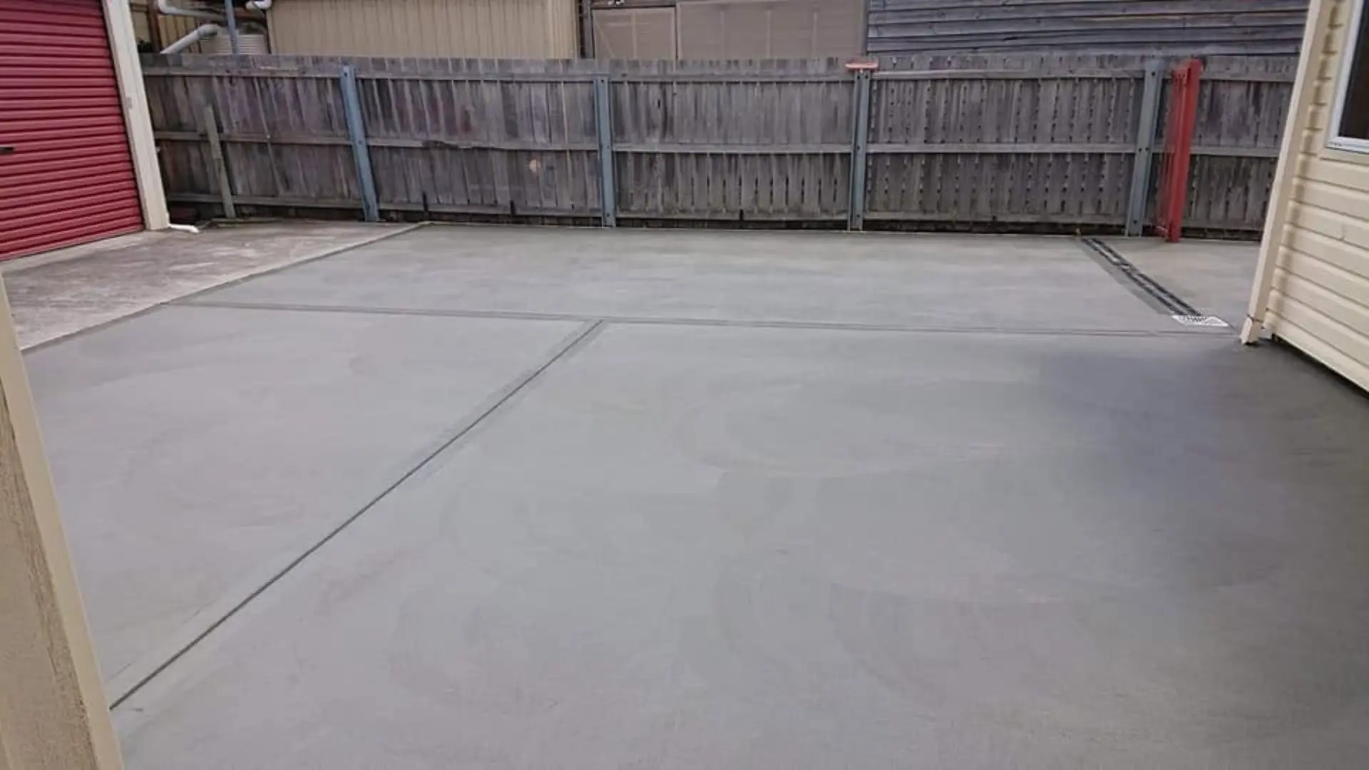 A wide finished concrete area laid between a house and paling fence
