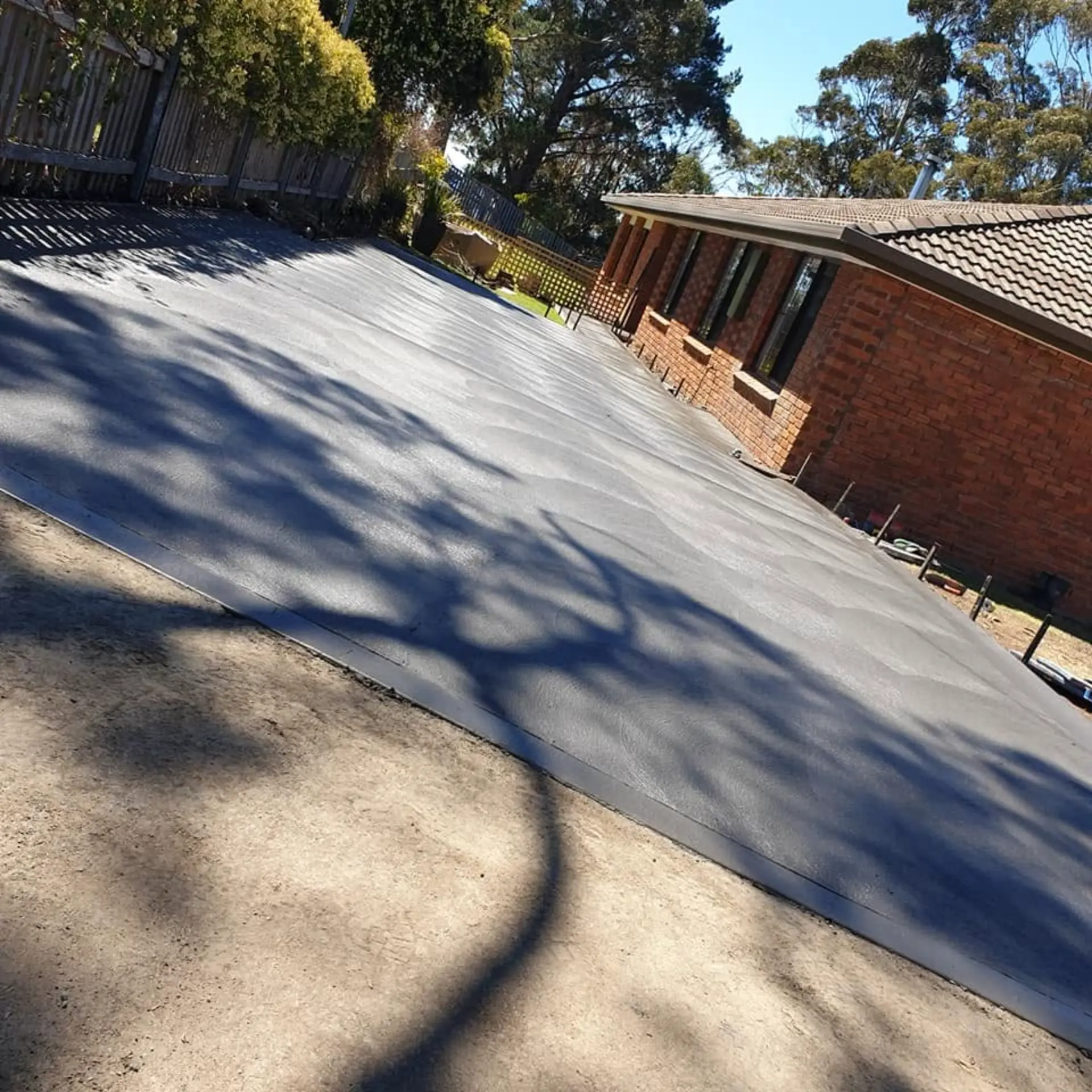 A finished concrete area laid beside a brick home in dappled sun